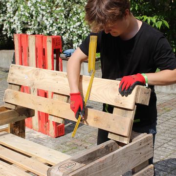 Eine Person misst die Lehne einer Bank aus Paletten nach.