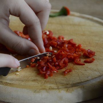 Eine Person schneidet Peperoni klein.